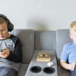 Two children using electronic devices near the Aires Tech Lifetune Zone Max EMF protection device placed on a couch armrest