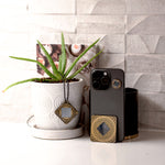 Phone case with decorative elements next to a potted plant on a surface.