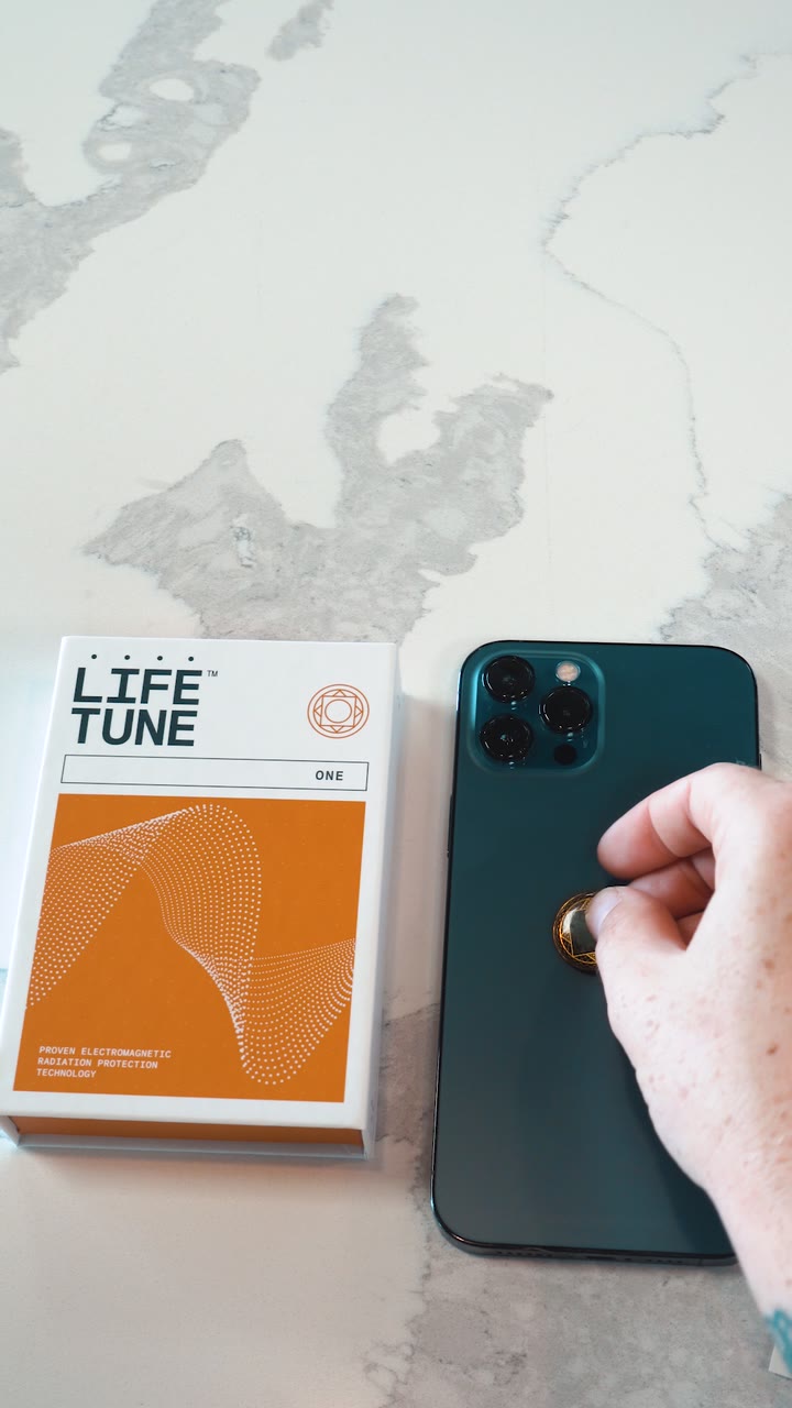 A hand pressing a Lifetune One onto the back of a phone, next to its box